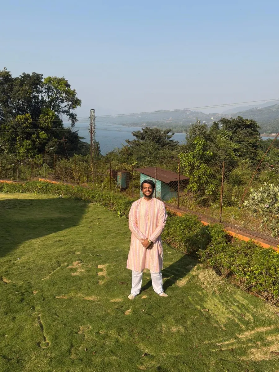 Prithvi in a pink kurta on a lawn above a lake and hills